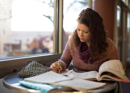 Female student with dark hair, scarf, and sweater, studies next to a window